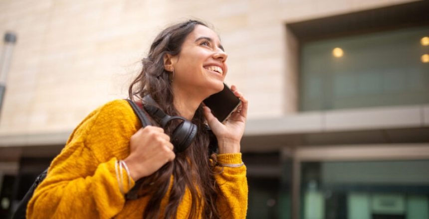Side portrait smiling woman walking and talking with cellphone in city