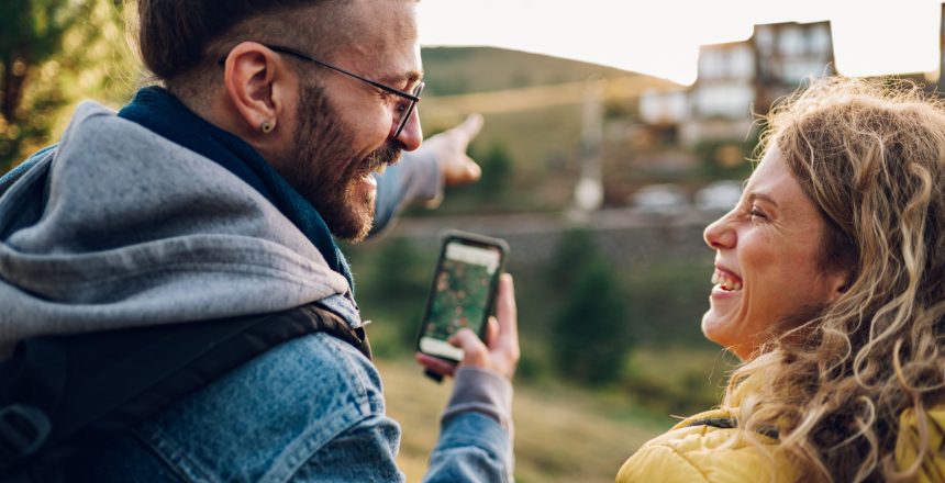 Cropped shot of a woman and man travelers enjoying hike and nature view while using maps on a smartphone to navigate. Couple walking on a mountain path during their vacation and using mobile phone.